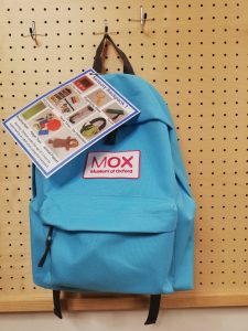 A blue rucksack with a pink MOX logo on it. Attached to the backpack is a label with pictures of the contents.