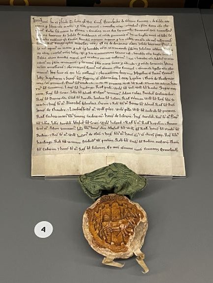 Document written in latin with an ornge coloured circular seal depicting a walled city, including three towers, an ox walking from left to right and the assertive legend (in Latin): ‘The common seal of all the citizens of the City of Oxford.
