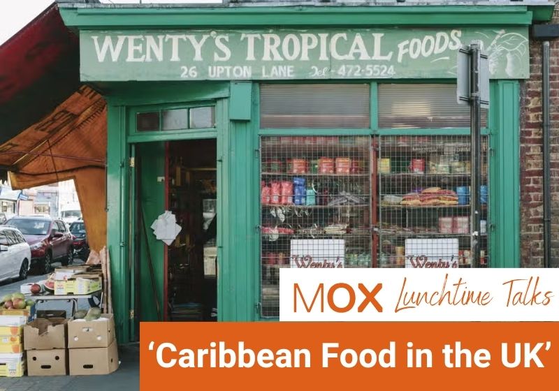 An image of a green shopfront with an open door. Handpainted white lettering on the storefront reads 'Wenty's Tropical Foods'. The shop windows are full of tinned pantry items. Outside the door and to the left are stacked crates of fresh produce. Text overlaid on the image reads 'MOX Lunchtime Talks. 'Caribbean Food in the UK''.