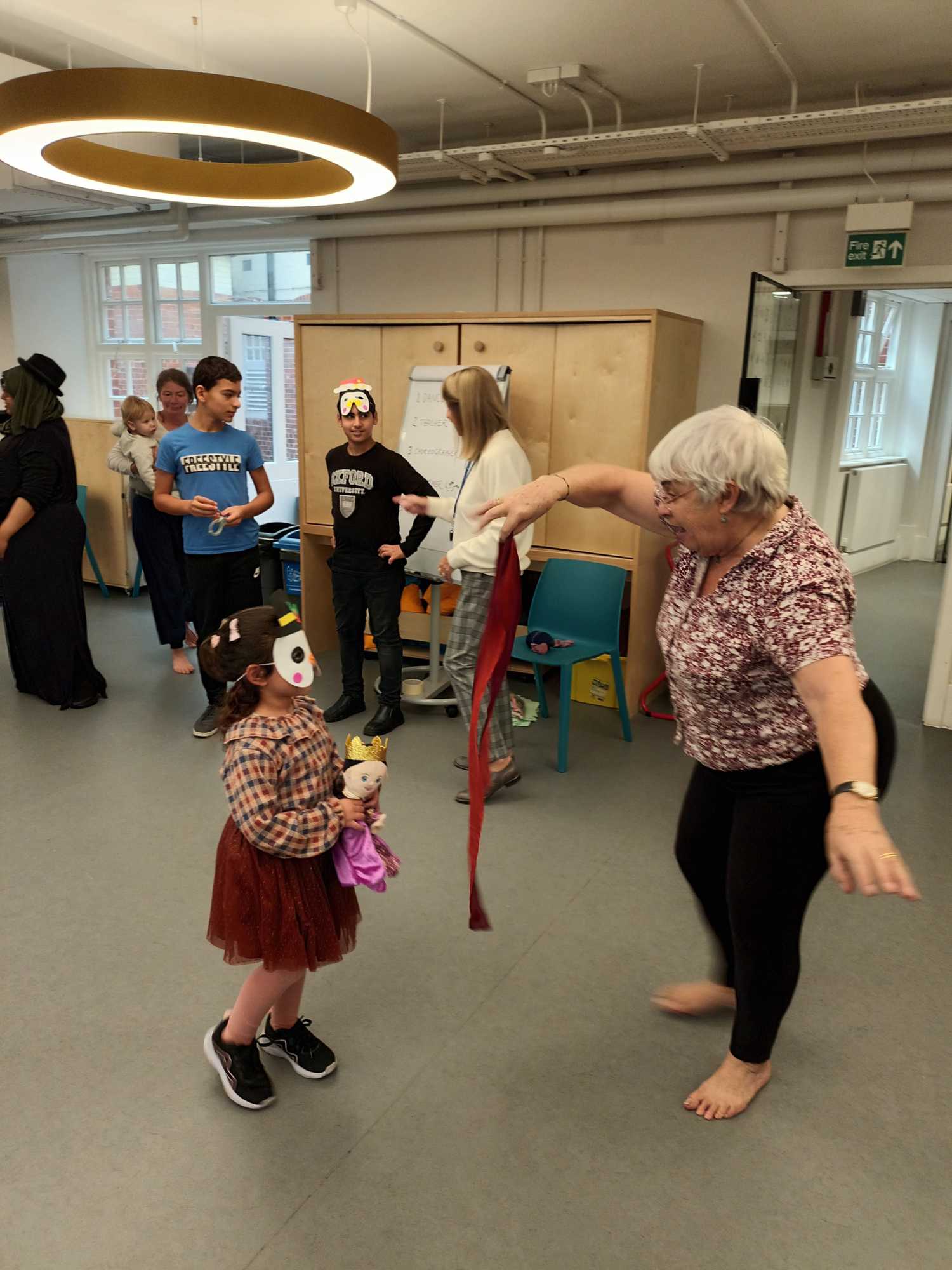 An older woman holds a streamer and entertains a young child, who is wearing an animal mask.