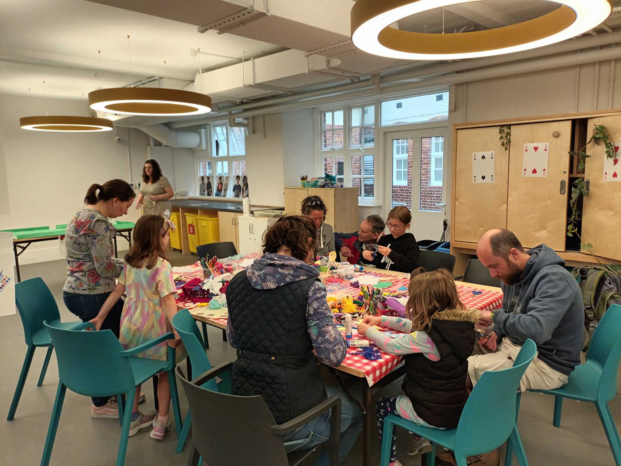A group of children and adults sit around a large table and engage in craft activities.