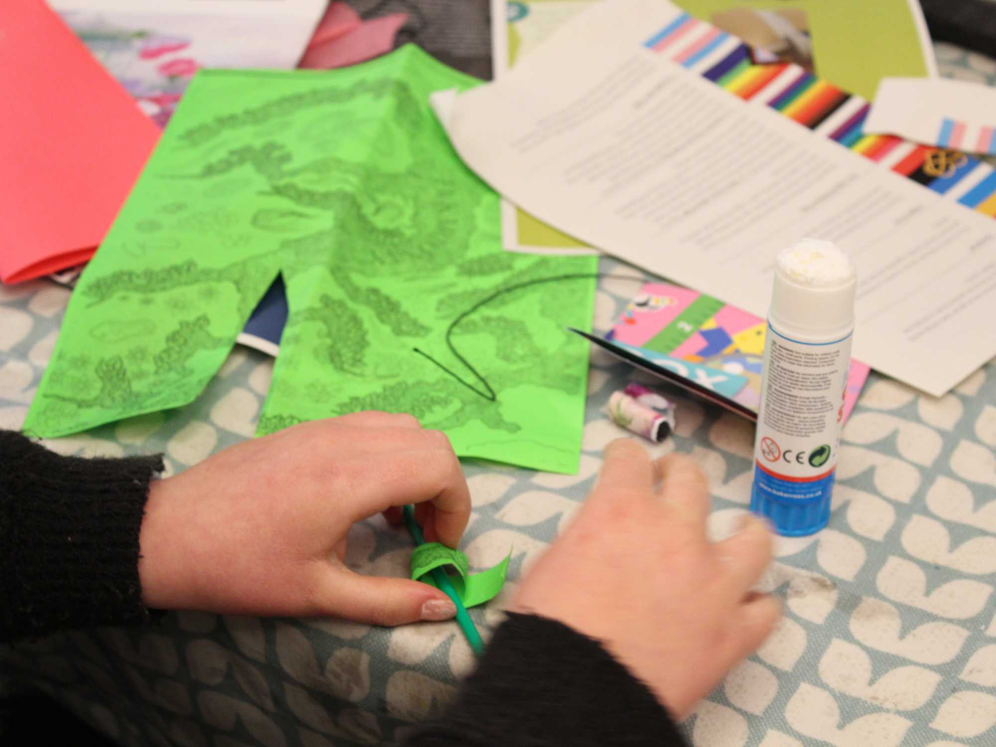 A table full of craft materials, including paper and glue. A child's hands interact with the materials.