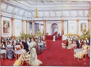 A grand room with a red carpet and people wearing Victorian clothing socialing