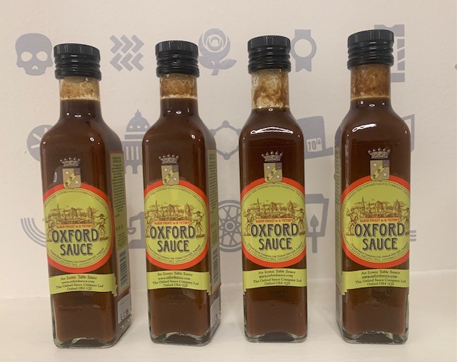 Four bottles containing brown liquid with a yellow label printed with Oxford Sauce