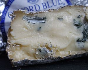 A photograph showing a portion of cheese with some of the wrapping visible which reads Oxford Blue