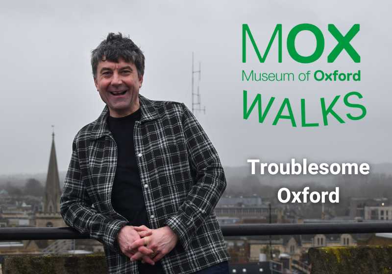 Maurice East smiles widely and leans against a railing in front of a view of the Oxford skyline on a cloudy day. Next to him is text which reads 'Museum of Oxford Walks. Troublesome Oxford'.