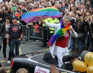 Photo of man in car surrounded by crowds waving the rainbow coloured Pride Flag