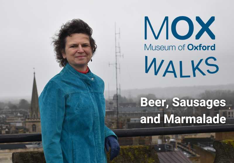 Liz Woolley stands next to a railing in front of a view of the Oxford skyline on a grey day. Text reads: 'Museum of Oxford Walks: Beer, Sausages and Marmalade'